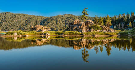 A wide shot of clean river surrounded with big rocks and green trees with a clear blue sky during daytimeの写真素材
