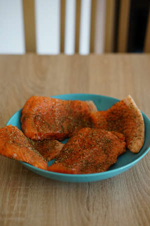 A vertical high angle closeup shot of the pieces of a raw salmon with species in a blue bowl on a wooden surfaceの写真素材