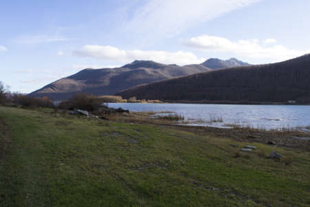 a panoramic shot of a grassy shore line with hills in the backgroundの写真素材