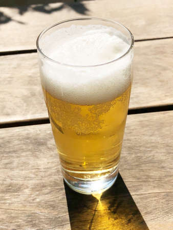 A vertical shot of a glass of cold beer on a wooden surfaceの写真素材