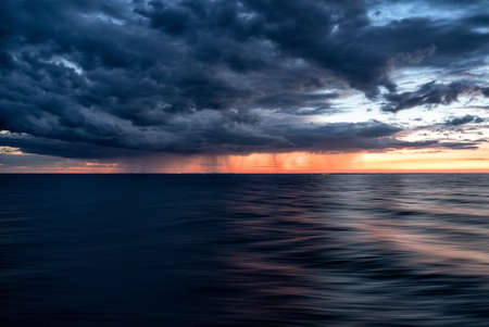 The dark clouds of the sunset sky over the dark water of the ocean