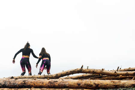 Young beautiful athletic female twins training on a pile of tree logs in the early morning - healthy lifestyle conceptの写真素材