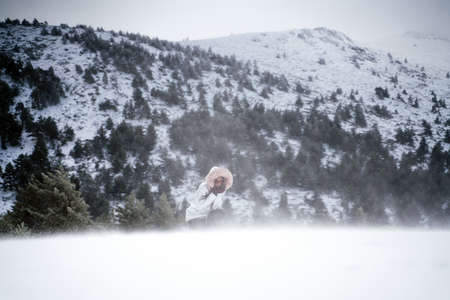 A low angle shot of a woman crouching in the middle of a snowy valley in winter