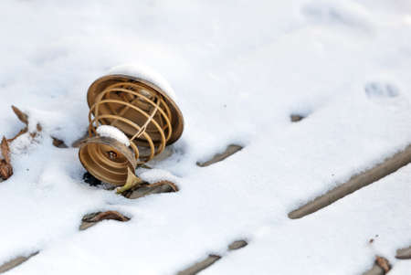A brown lamp made of wood tossed on the snow next to a leaf in winter