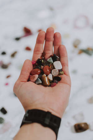 A closeup shot of a hand that holds many small rocks with multiple colors
