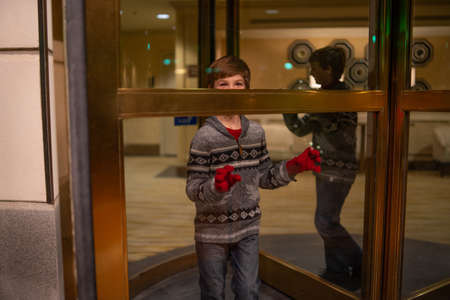 A cute boy in red gloves posing while standing behind the entrance doorの写真素材