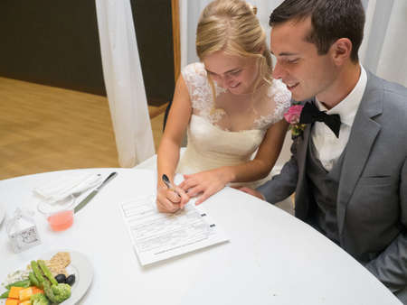 A just-married couple signing a prenup paper on a white table under the lightsの写真素材
