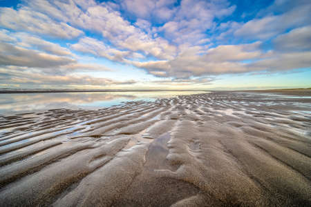 A beautiful shot of a wet sandy shore near water under a blue cloudy sky