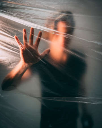 A man behind a plastic bag touching it with his palm