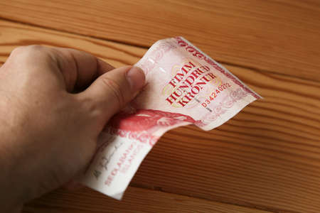 A high angle shot of a person holding a banknote over a wooden surface