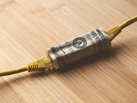 A closeup shot of two yellow internet cables going through a dollar bill on a wooden surface