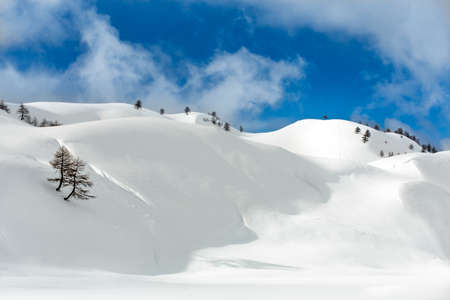 A landscape shot of hills covered with snow in a cloudy blue skyの写真素材