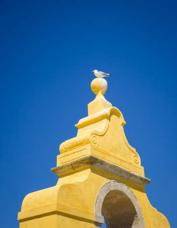 A low angle shot of a seagull perched on top of a yellow tower under the clear blue skyの写真素材