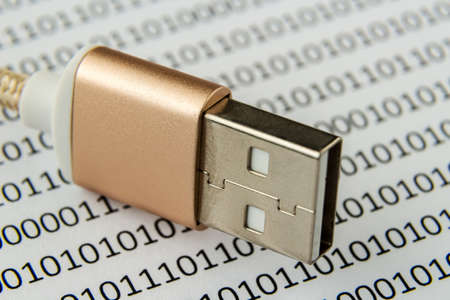 A closeup shot of a USB cable on a piece of paper with numbers and codes written on it