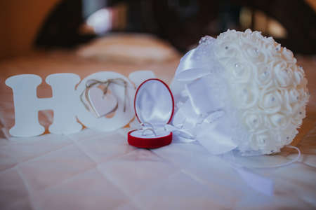 A closeup shot of wedding rings in a red box and a white bouquet with a blurry backgroundの写真素材
