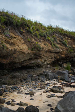 A vertical shot of a cliff covered with green grass near a lot of black rocks