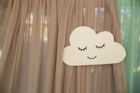 A closeup of a handmade paper cloud with a face on the curtains under the lightsの写真素材