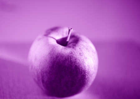 A closeup of an apple on a table under the lights with a blurry background and a purple effectの写真素材