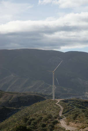 A majestic view of a dirt road on a valley  with a windmill on a cloudy day