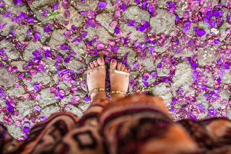 A high angle shot of a female's feet on a concrete ground covered with fallen flowers petals