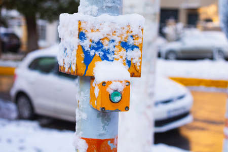 A closeup of a yellow traffic light button covered in the snow with the road on the backgroundの写真素材