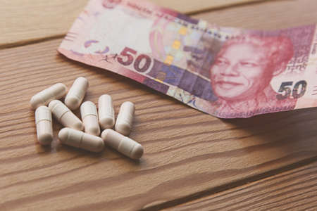 A high angle shot of some capsules and a South African 50 rand cash on a wooden table