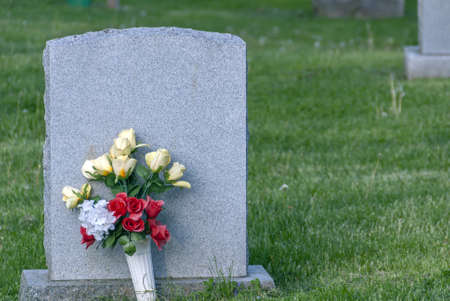 Flowers put on a concrete grave surrounded by green grassの写真素材