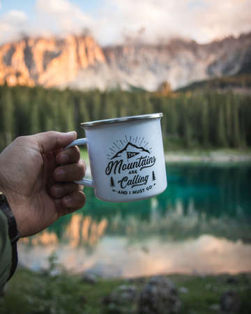 A hand holding a white mug with a blurry mountain landscape as backgroundの写真素材