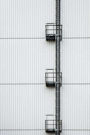 A vertical shot of a tall white building with a ladder on the sideの写真素材