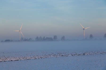 A snowy field with windmills in the distance at winter