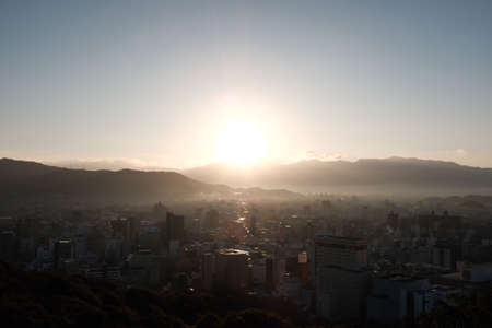 A city surrounded by hills covered in greenery under a blue sky during the sunsetの写真素材