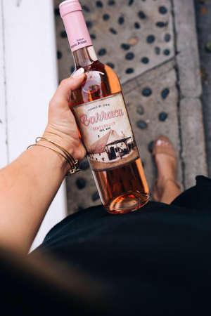 SAN CLEMENTE, UNITED STATES - Nov 22, 2018: A vertical photo of a woman standing while holding rosÃ© wine bottle in hand, taking a step.のeditorial素材