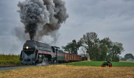 STRASBURG, UNITED STATES - Oct 06, 2019: Steam Freight Train Passing an Antique Tractor with a Woman...