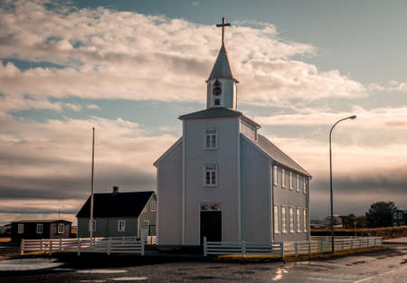 A white church with a cross on the top and beautiful clouds in the background