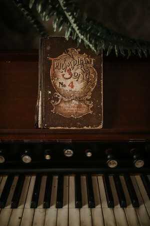 A vertical closeup shot of a vintage piano and a sheet music book that says Triumphant Songs