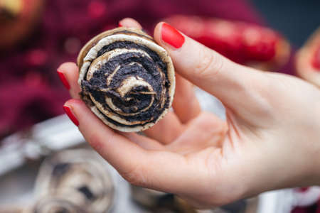 A close shot of a raw vegan poppy roll in the hands of a woman with red polished nailsの写真素材
