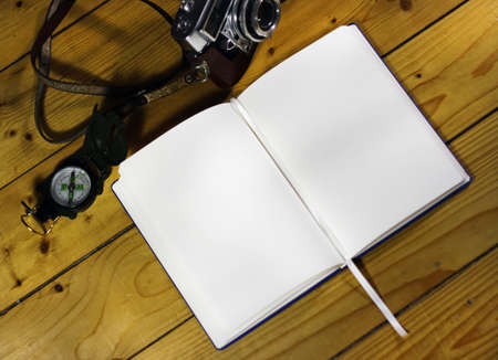 An open notebook next to a watch and camera on a wooden surface