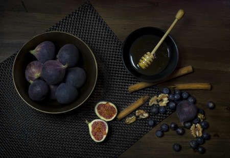 A high angle view of a bowl of figs with honey walnuts and blueberries on the table
