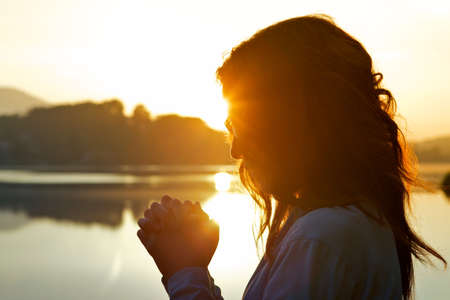 A praying woman surrounded by the lake and hills under the sunlight during the sunsetの写真素材