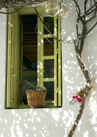 An old taverna white wall with a green window and a tree next to it in Folegandros, Greeceの写真素材