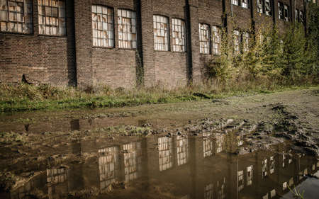 An old abandoned stone building with broken windows and a puddle outsideの写真素材