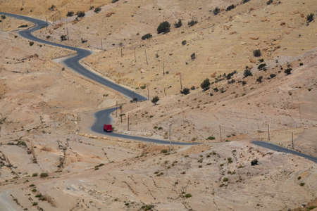 A car going on a road over a mountain of sand and tiny bushes during daytime