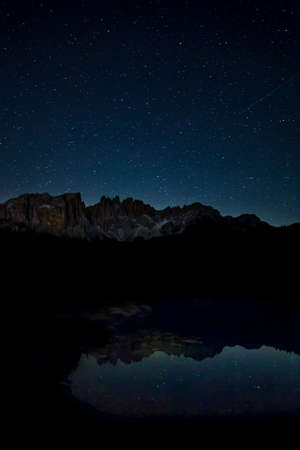 A breathtaking scenery of the starry sky and rocky cliffs reflecting on the lake at night time