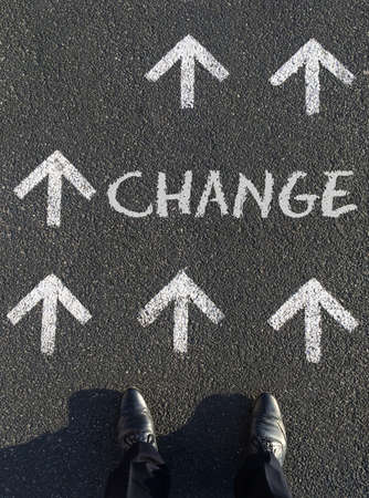 A vertical shot of a man standing in front of the word Change written on the ground surrounded by arrowsの写真素材