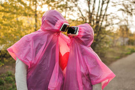A closeup shot of two people romantically looking at each other in pink plastic raincoats and VR...