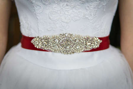 A closeup shot of a wedding dress with a beautiful red belt with precious stones