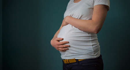 A pregnant woman in a white shirt holding her belly