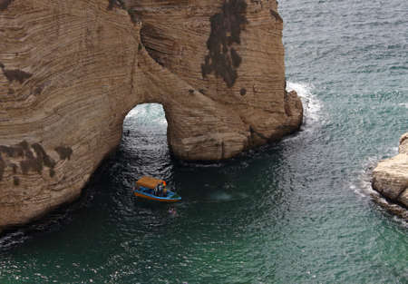A high angle shot of a boat sailing on the water next to a large cliff