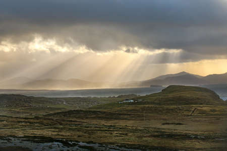 A beautiful shot of the fields and mountains with sun rays shining through cloudsの写真素材