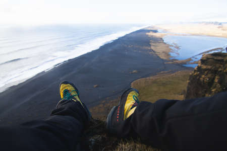 A closeup of legs of a person sitting on the rock with the sea on the blurry background in Iceland